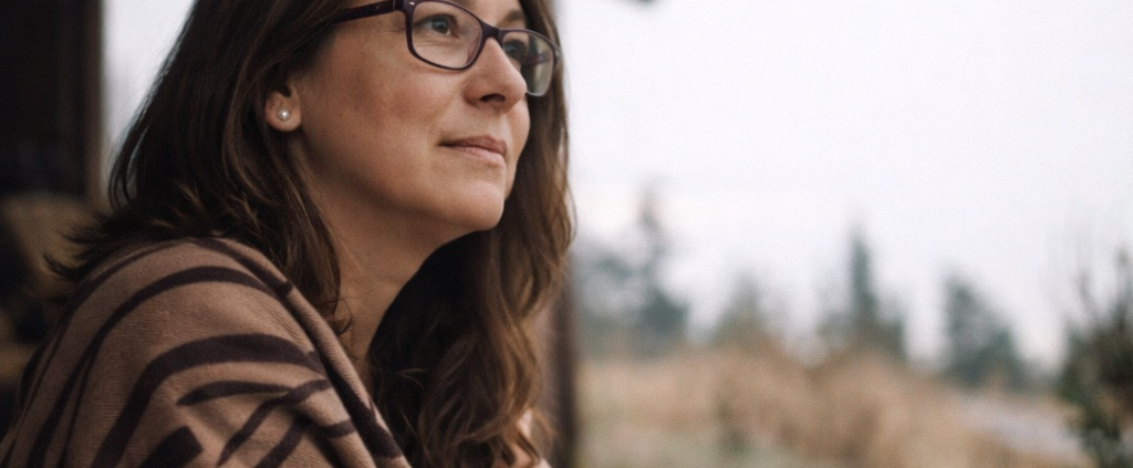 Nachdenkliche Frau sitzt vor einem rustikalen Holzhaus und blickt in die Ferne – symbolisch für innere Reflexion und das Lösen von Konflikten